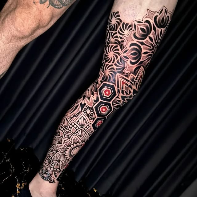 Geometric mandala leg sleeve tattoo in black and grey with red accents